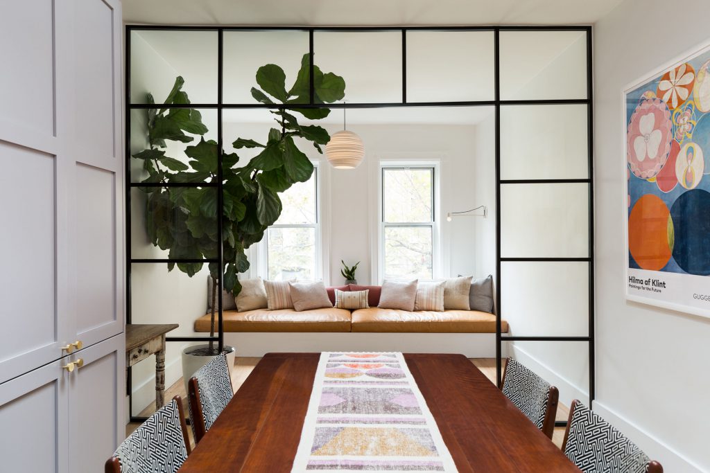 a long wooden table in front of a living area with a glass partition
