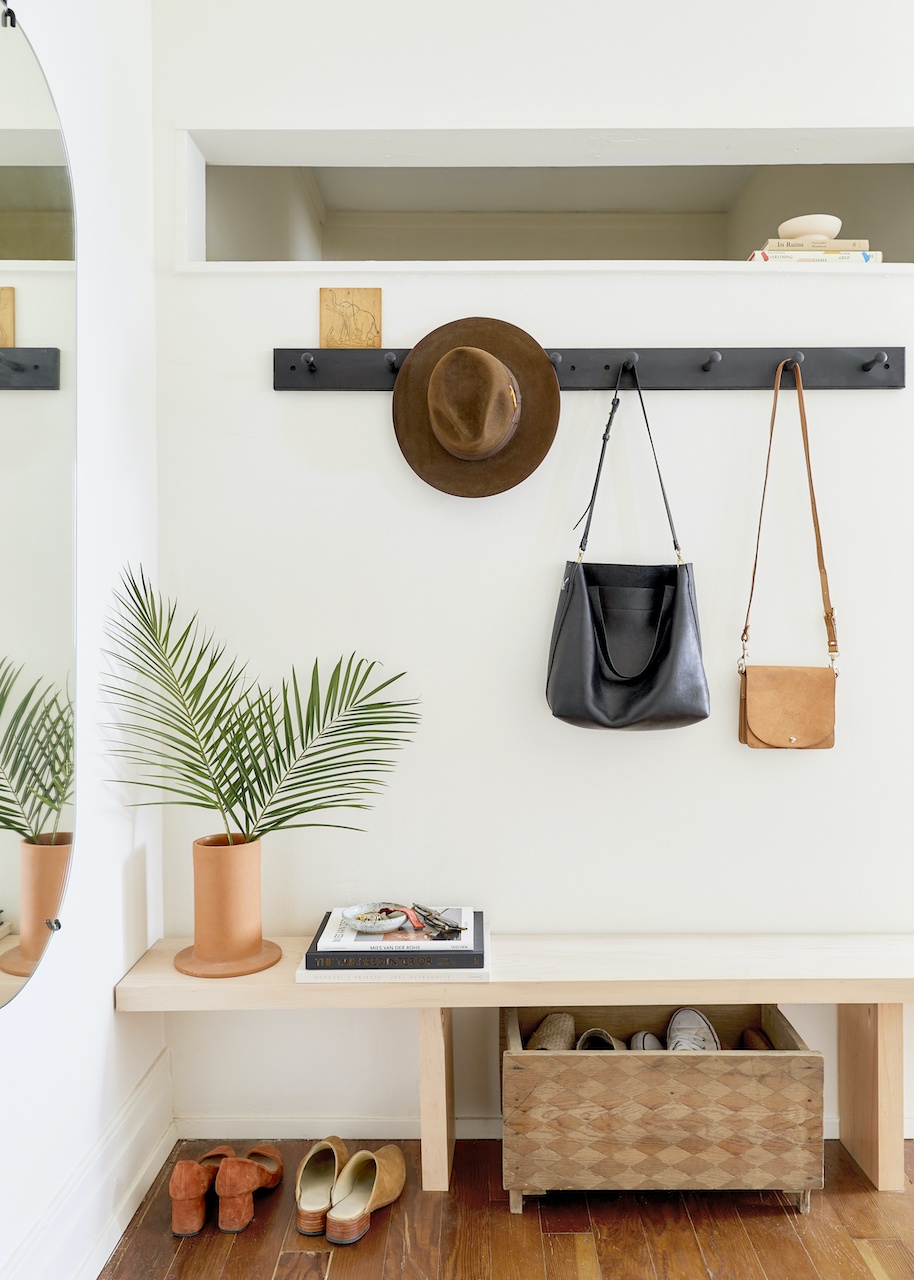 a neutral-colored entryway with a bench, hung bags, and shoes.