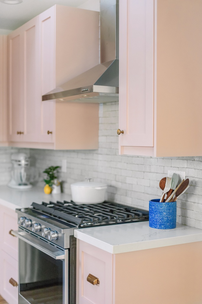 the oven and hood surrounded by pink cabinets