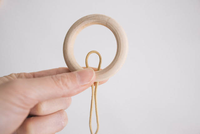 Cut a piece of leather cord to 48 inches long. Fold it in half and place the center loop behind a wooden hoop.