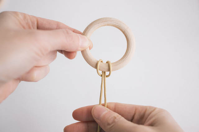 Pull the two loose ends of the cord through the leather loop to attach it to the wooden hoop.