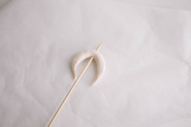 Pinch and smooth the ends to form a pointed crescent. Then thread a skewer through the center to form holes on the top and bottom.