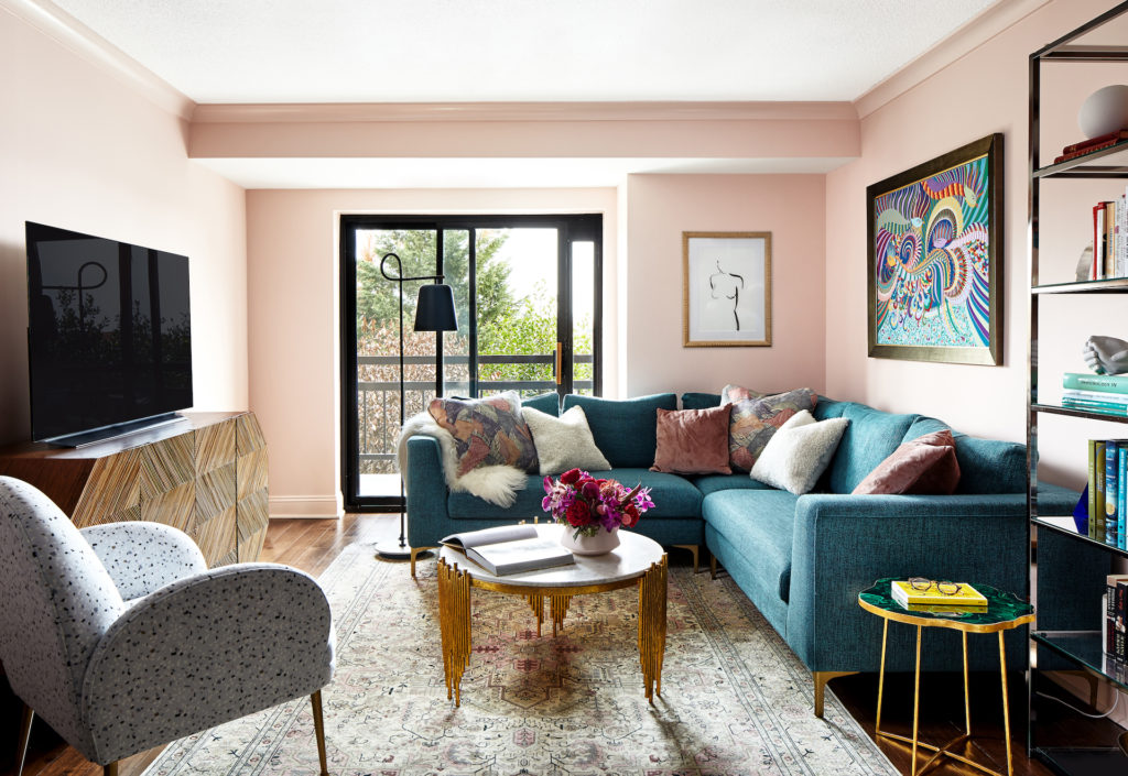 a living room with pink walls and a teal sectional leading to a balcony outside