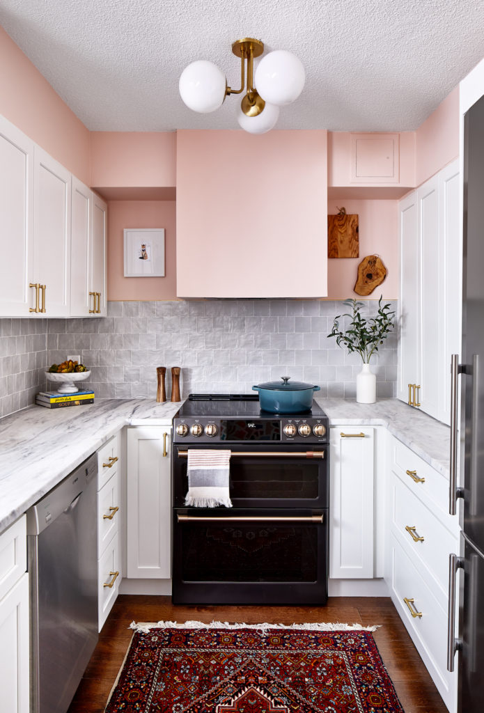 a kitchen with pink walls, a gray backsplash, white cabinets, and a black stove.