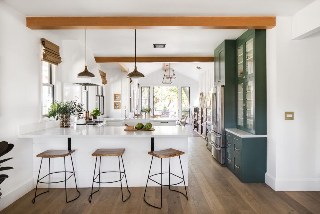 the kitchen, with three wooden stools at the peninsula, white cabinets, and a green bank of cabinets on the right wall.