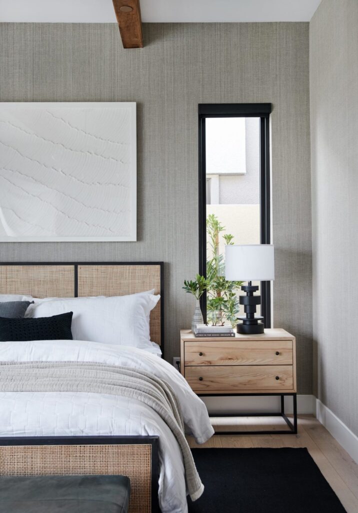 a neutral bedroom with gray walls, a light wood nightstand, a cane bedroom, white sheets, and a black-framed window