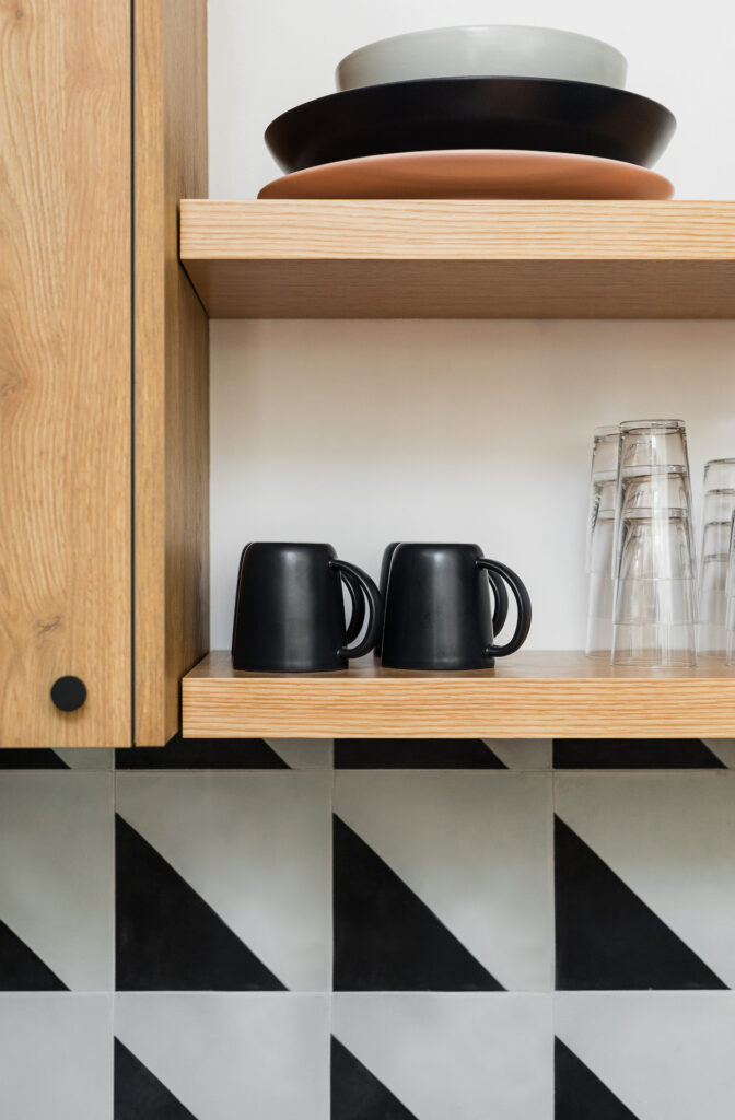 a close up of the black and white tile backsplash, open shelving, and black coffee mugs