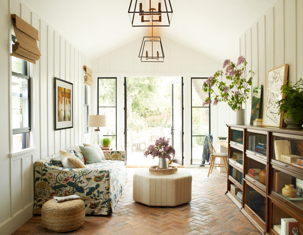 a sunroom with a floral couch, brick floors, and tall windows and ceilings.
