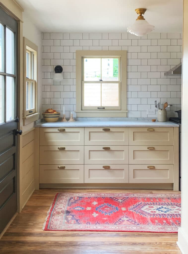 Cream cabinets in a kitchen with subway tile and pink rug