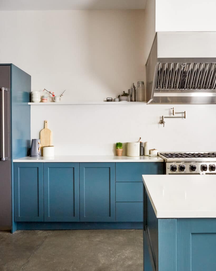 Blue kitchen with white counters and walls and shelf